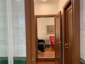 A hallway with a wooden door, a tiled wall, a red chair, and a small table with a lamp. - SmooRoomS Trastevere (Rome)