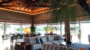 A spacious indoor area with a high ceiling, a large sofa set, a dining area with chairs, and a large potted plant. - Buganville Villas (Itai)