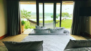 A bedroom with a large bed, a view of a grassy landscape, and a hammock outside the window. - Buganville Villas (Itai)