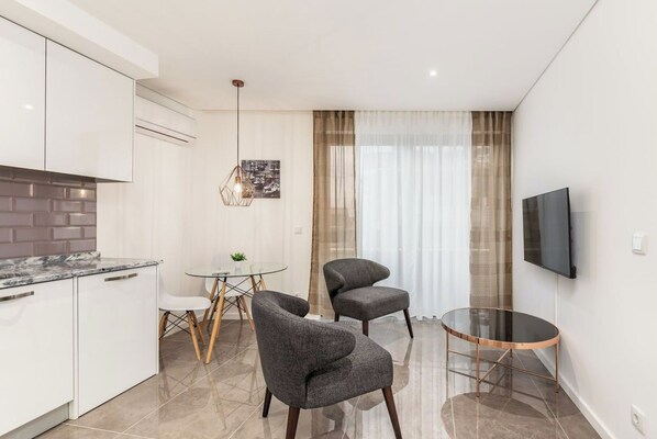 A modern kitchen with white cabinets, a marble countertop, and a dining area with two grey chairs and a glass table.