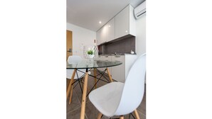 A modern kitchen with white cabinets, a glass dining table, and a white chair. - APARTMENT 2 / BALCONY (Espinho)
