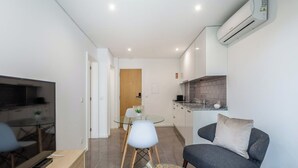 A modern living room with a TV, a sofa, a coffee table, and a kitchen area with a sink and countertop. - APARTMENT 2 / BALCONY (Espinho)