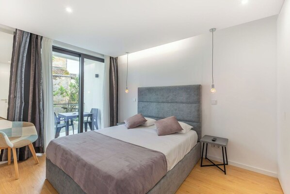 A modern bedroom with a large bed, a small desk, and a balcony with a table and chairs.