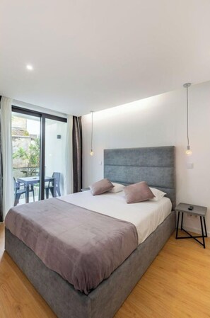 A modern bedroom with a large bed, a small bedside table, and a view of an outdoor area with a table and chairs.
