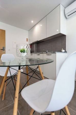 A modern kitchen with white cabinets, a glass dining table, and a white chair.