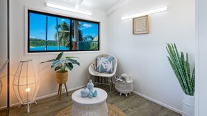 Una habitación con un ventanal grande, una silla de ratán, una lámpara de pie de mimbre y una mesita redonda con adornos.