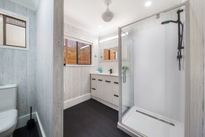 A modern bathroom with a glass-enclosed shower, a toilet, and a vanity with a mirror. - Coral Sea Pearl (Shute Harbour)