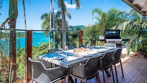 An outdoor dining area with a view of the ocean, a grill, and lush greenery. - Coral Sea Pearl (Shute Harbour)