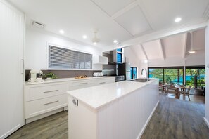 A modern kitchen with a large island, white cabinetry, and a view to a balcony. - Coral Sea Pearl (Shute Harbour)