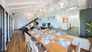 A modern dining area with a long wooden table set for a meal, a staircase leading to an upper level, and a view of the kitchen area. - Coral Sea Pearl (Shute Harbour)