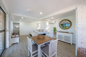 A modern interior with a dining area, a sofa set, and a kitchen in the background. - Coral Sea Pearl (Shute Harbour)