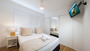 A bedroom with a bed, bedside table, lamp, and a wall-mounted TV. - Coral Sea Pearl (Shute Harbour)