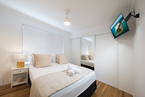 A bedroom with a bed, bedside table, lamp, and a wall-mounted TV. - Coral Sea Pearl (Shute Harbour)