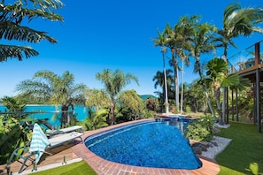 A swimming pool with a curved edge, surrounded by palm trees and a clear blue sky. - Coral Sea Pearl (Shute Harbour)