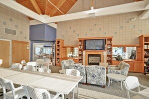A spacious room with a fireplace, bookshelves, and a television. There are several chairs and a table.