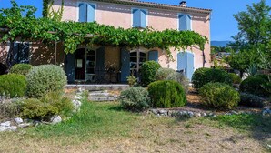Un bâtiment à deux étages doté d’un porche abrité, d’un escalier en pierre et d’un jardin agrémenté de divers arbustes et d’un petit arbre.
