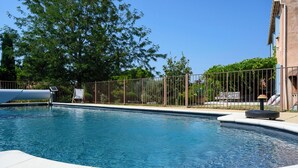 Une piscine avec une terrasse carrelée, une clôture en métal et un fauteuil de relaxation.