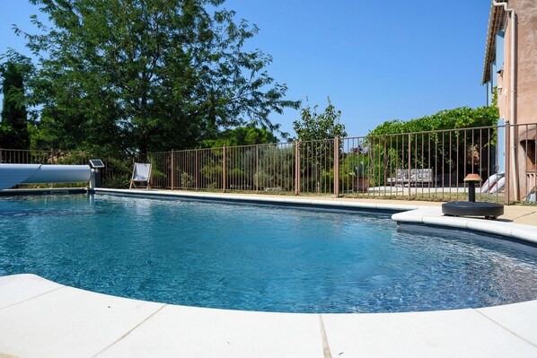 Une piscine avec une terrasse carrelée, une clôture en métal et un fauteuil de relaxation.