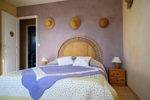 Une chambre à coucher avec un lit, deux tables de chevet et trois chapeaux en fibres tressées accrochés au mur.