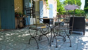 Une terrasse extérieure avec une table et des chaises, une porte bleue et un pot de fleurs.
