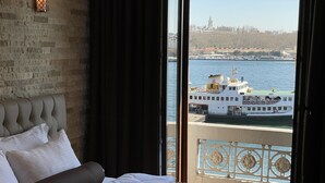 A hotel room with a bed, a view of a river, and a boat. - Weingart Seaside Hotel (Istanbul)