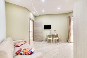 A living room with a sofa, colorful pillows, a dining table with chairs, a flat-screen TV mounted on the wall, and a sliding door. - Eclisse House Few Steps From The Sea (Augusta)