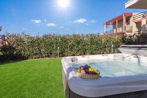 A hot tub with a basket of fruit on a well-maintained lawn, surrounded by a fence and a building with balconies. - Eclisse House Few Steps From The Sea (Augusta)