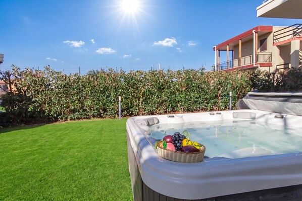 A hot tub with a basket of fruit on a well-maintained lawn, surrounded by a fence and a building with balconies.