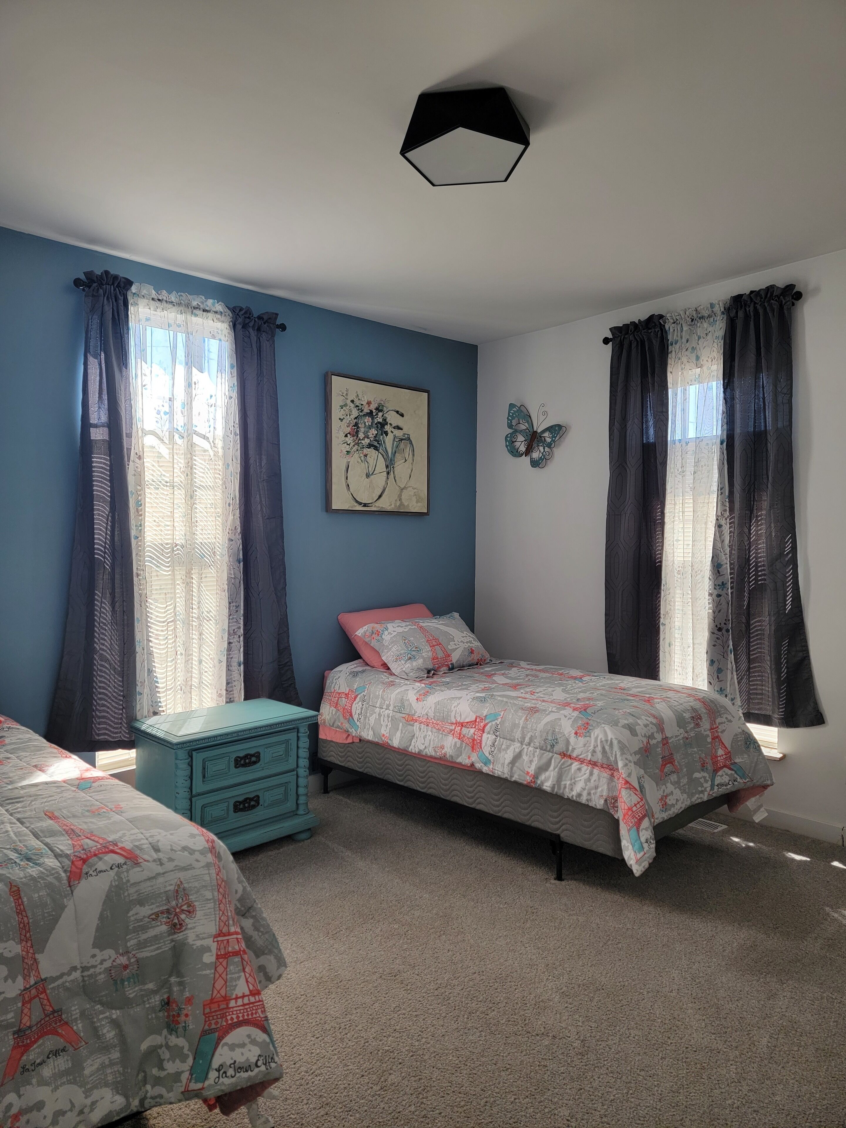 A bedroom with two beds, a dresser, a painting, and a butterfly wall decoration.