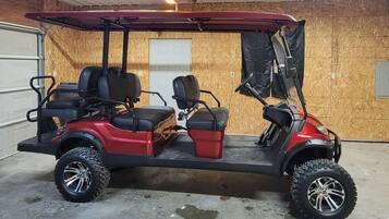 Um carrinho de golfe vermelho com dois assentos e um compartimento de armazenamento, estacionado em uma garagem com paredes de madeira e piso de concreto.