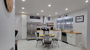 Een moderne keuken met witte kasten, een centraal eiland en een eethoek met een ronde tafel en stoelen.