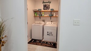 Een wasserette met twee wasmachines, een plank met wasmiddelen, en een bordje met de tekst 'Laundry Wash & Dry'.