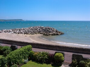 Une vue sur la côte, avec un brise-lames rocheux, une promenade dallée et une végétation luxuriante.