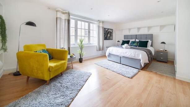 A modern bedroom with a bed, a yellow armchair, a large window, and a potted plant.