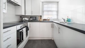A modern kitchen with white cabinets, a black countertop, a microwave, a stove, and a sink.