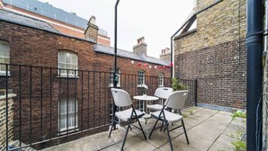 A courtyard with a brick wall, a metal fence, and a small table with chairs.