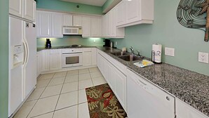 A compact kitchen with white cabinets, a microwave, a sink, and a dishwasher. - Spacious Gulf Front Condo - Stunning Views + On-Site Amenities! (Navarre Beach)