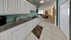 A kitchen with white cabinets, a granite countertop, and a tiled floor. - Spacious Gulf Front Condo - Stunning Views + On-Site Amenities! (Navarre Beach)