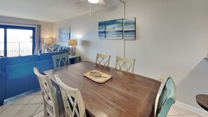 Un comedor con una mesa de madera, cuatro sillas, un ventilador de techo y vista al océano a través de un ventanal.