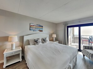 Una camera da letto con un letto grande, due comodini con lampade, un quadro appeso al muro e un balcone con sedie.