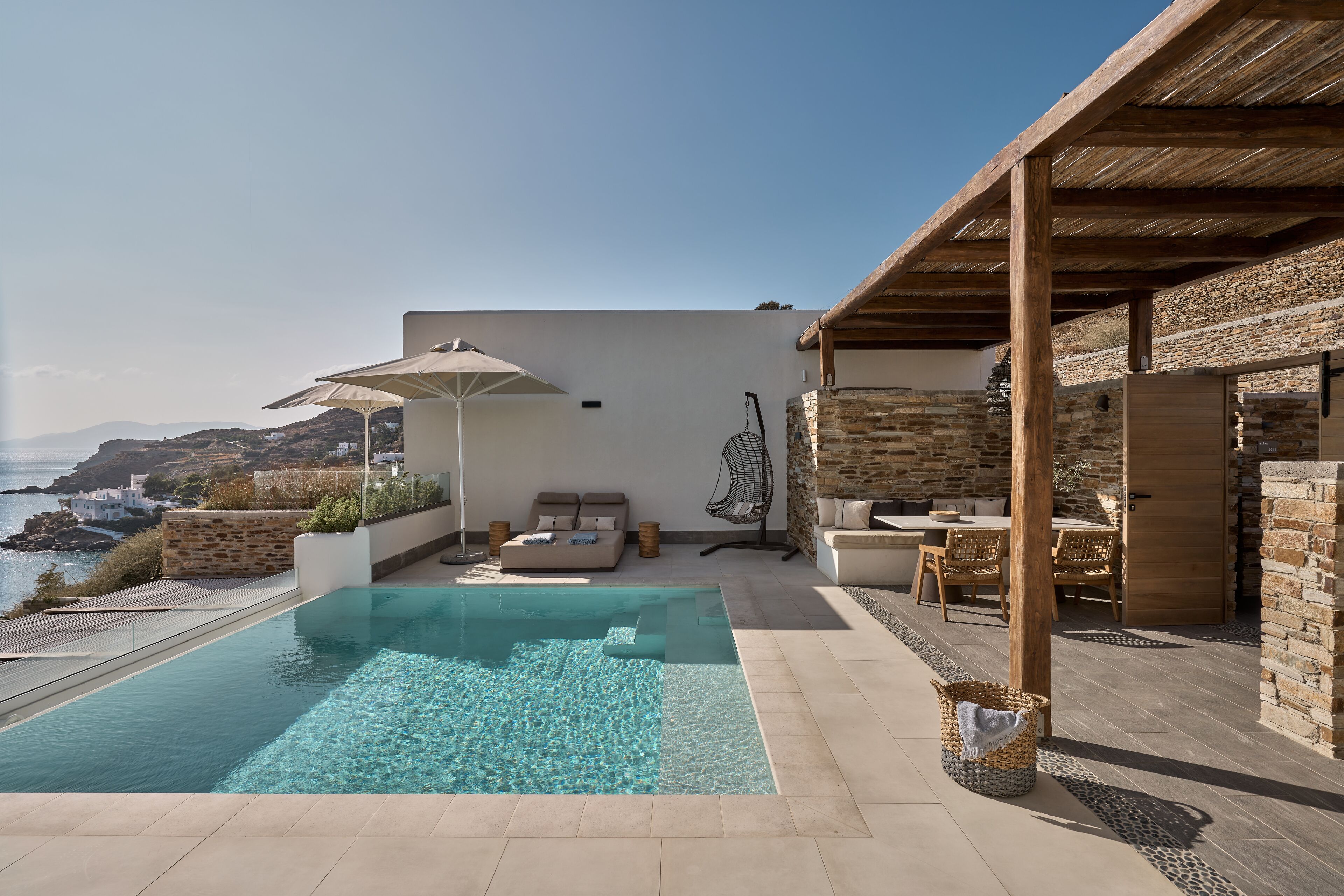 A poolside area with a clear pool, outdoor seating, and a view of the sea.