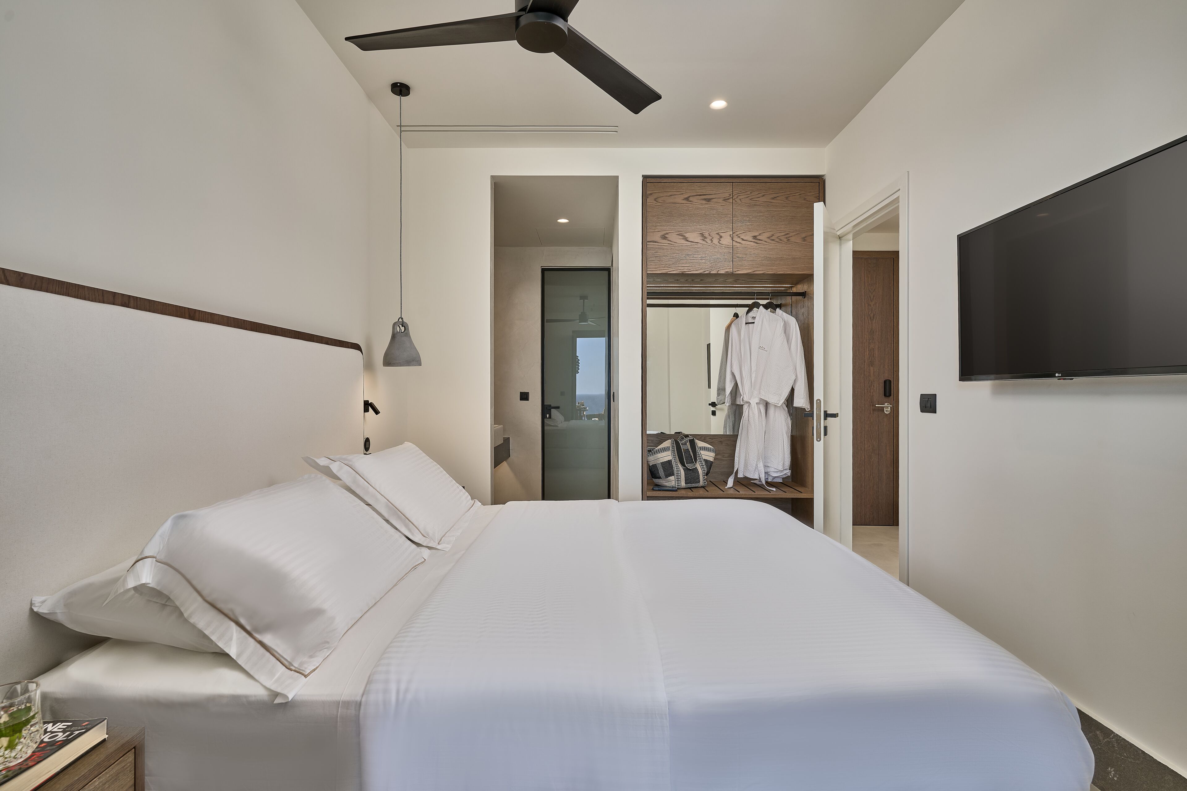 Ein modernes Hotelzimmer mit einem großen Bett, einem Deckenventilator, einem Flachbildfernseher und einem begehbaren Kleiderschrank.