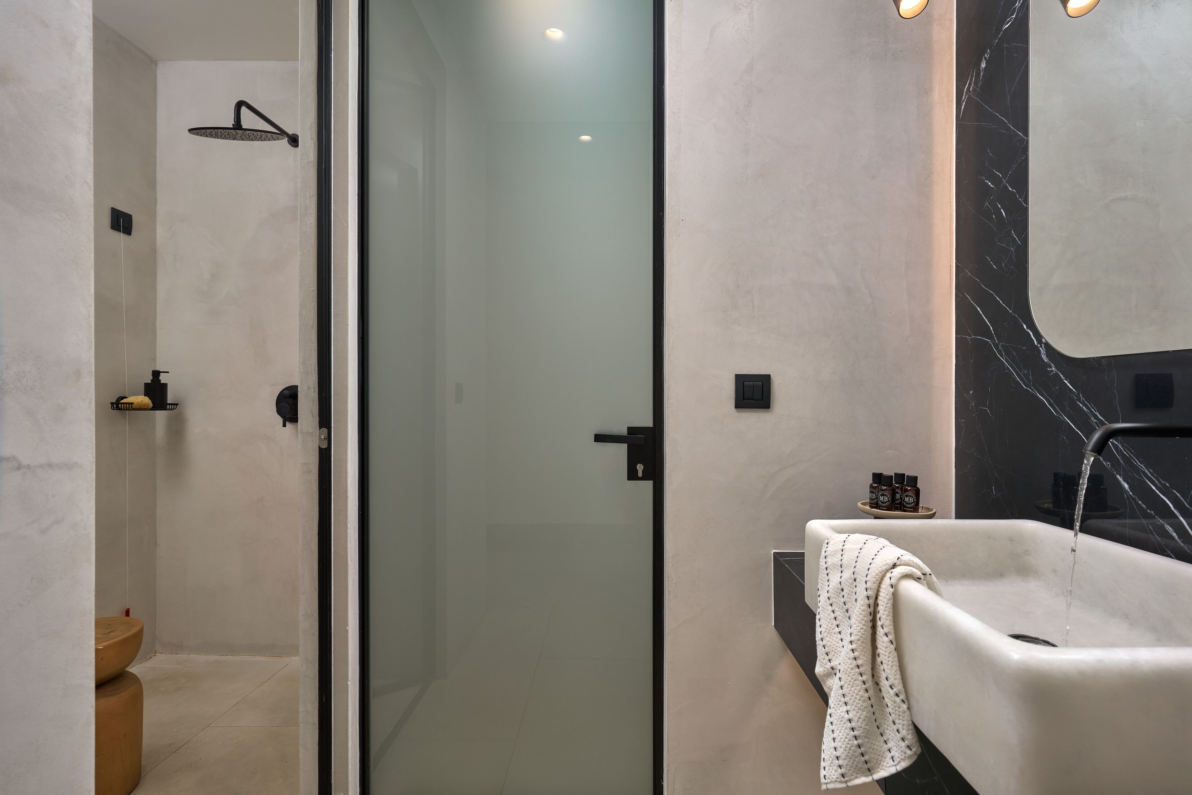 A modern bathroom with a glass-enclosed shower, a marble-tiled wall, and a white sink with a towel.