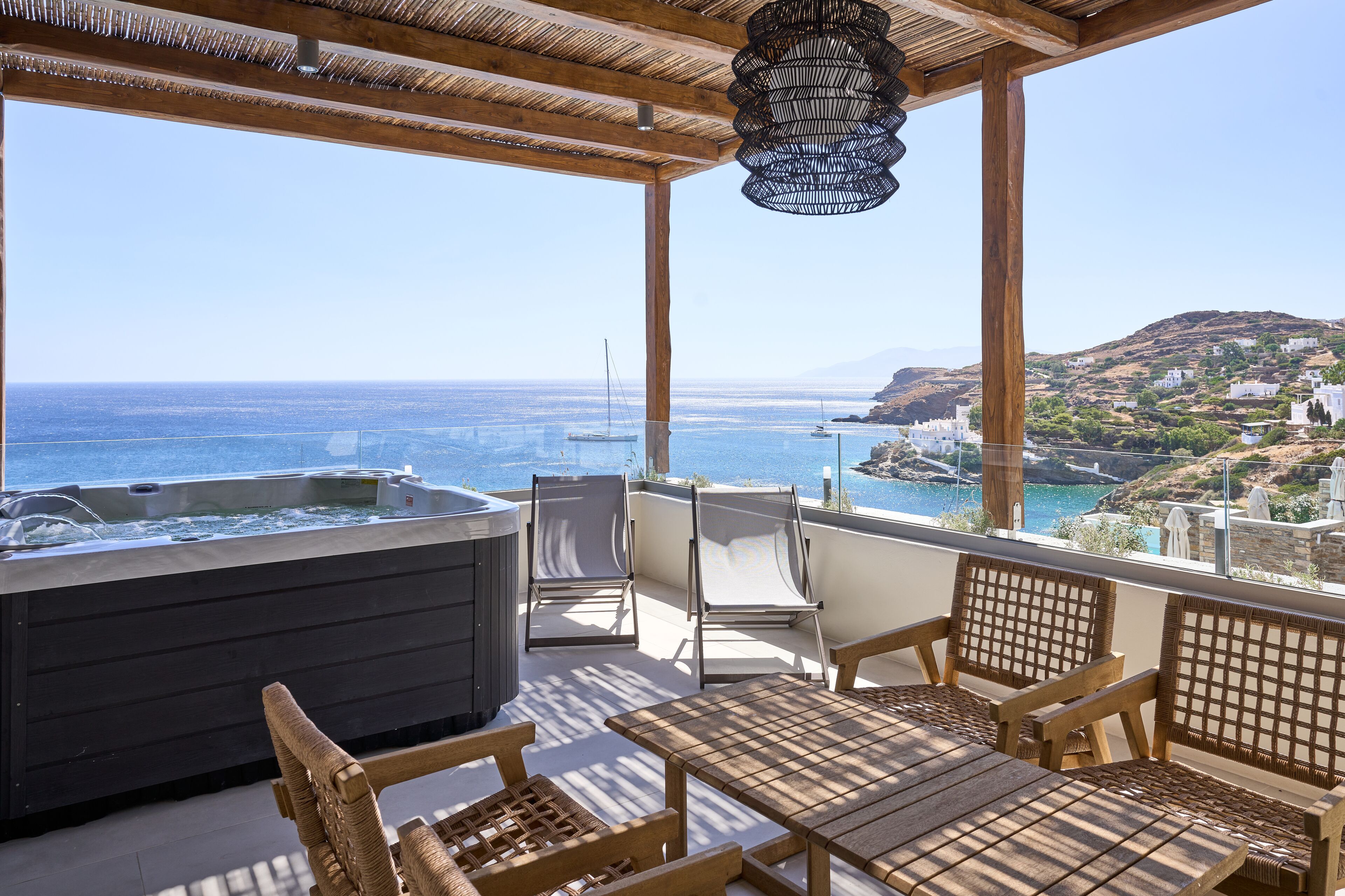 A balcony with a hot tub, wicker furniture, and a view of the sea and hills.