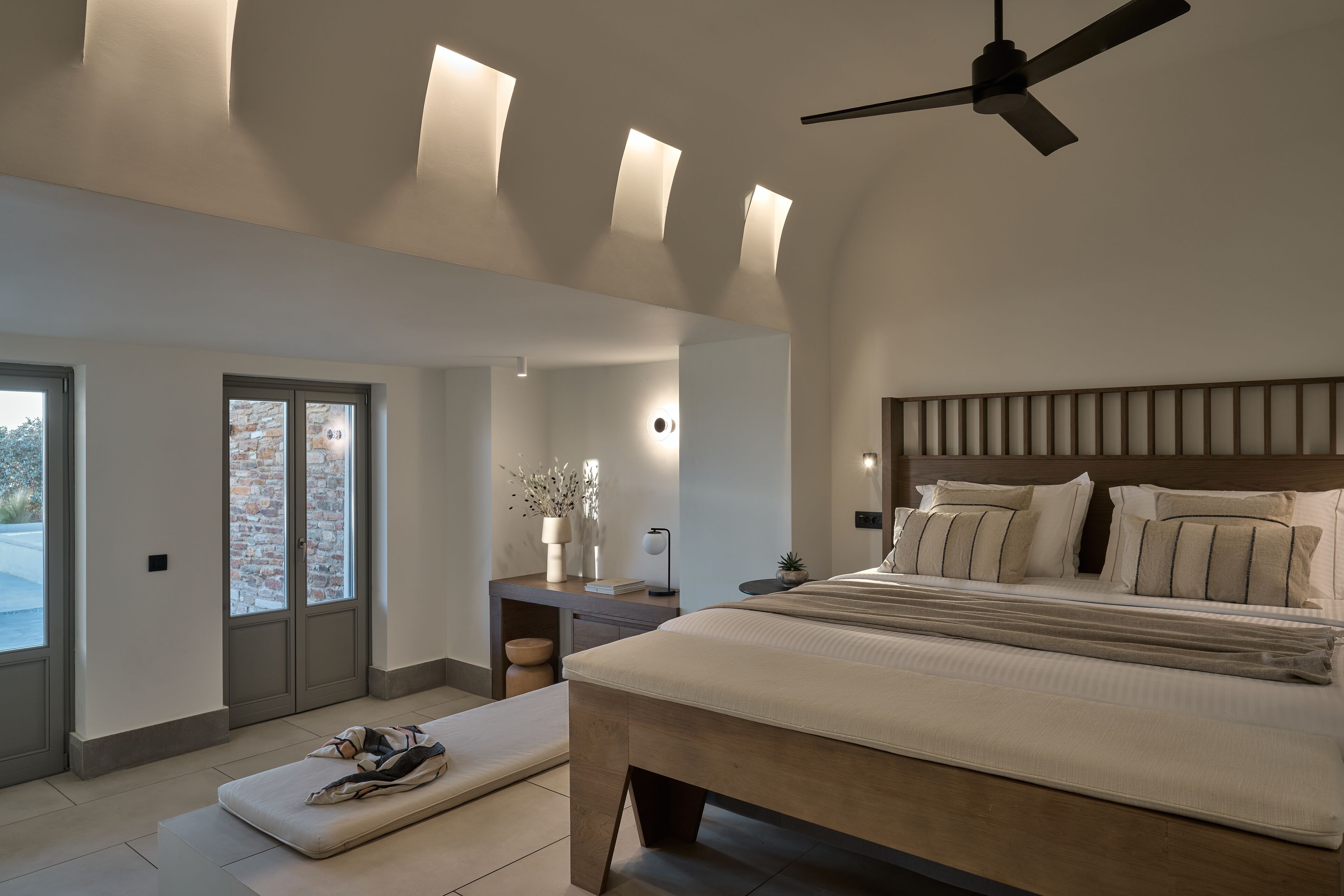 A modern bedroom with a large bed, a ceiling fan, and a view of the outdoors through a sliding door.