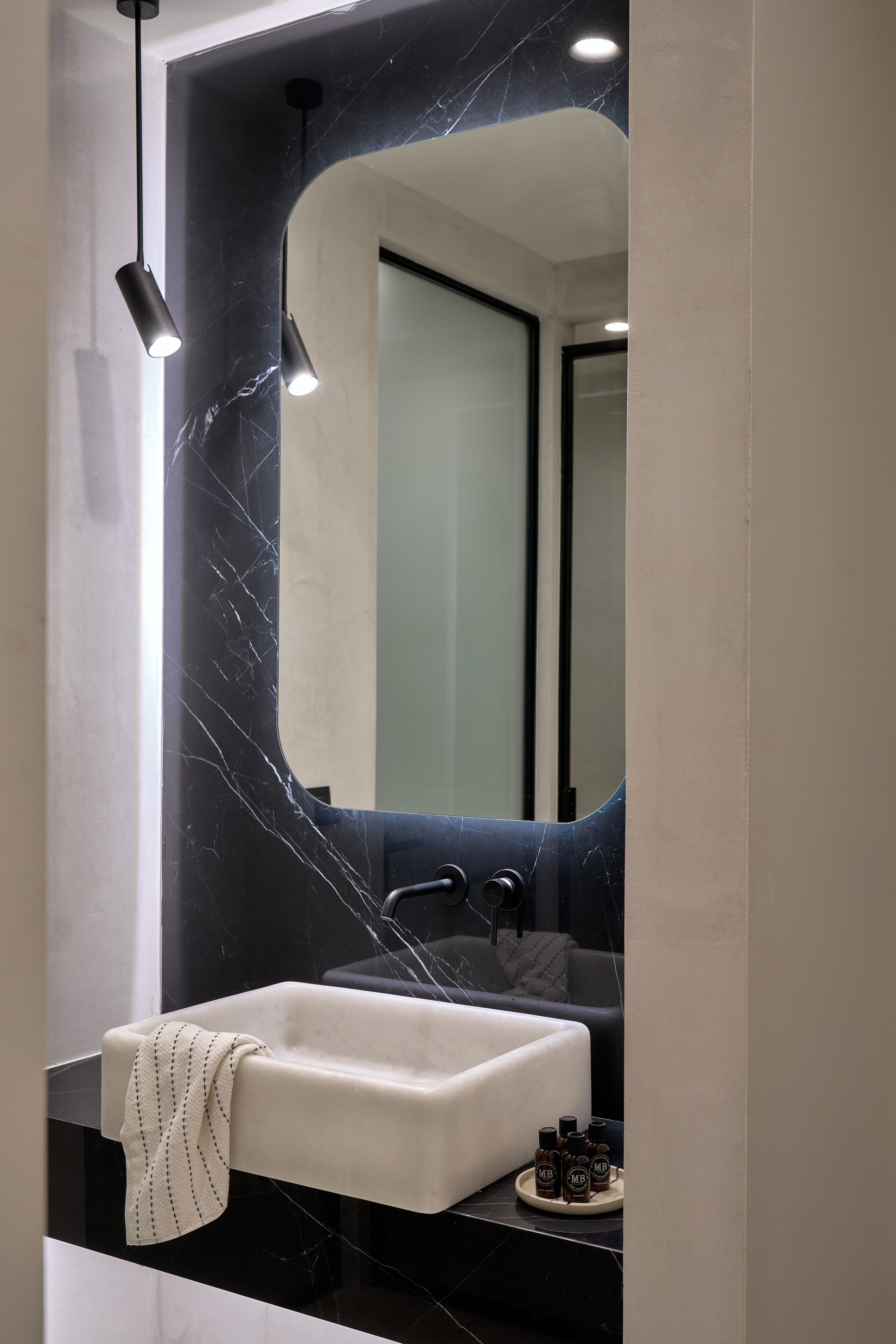 A modern bathroom with a white sink, black marble backsplash, and a large mirror.