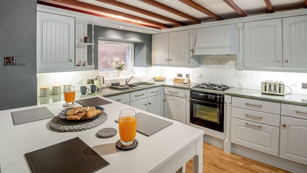 Eine moderne Küche mit weißen Schränken, einer Holzbalkendecke und einem Essbereich mit einem für das Frühstück gedeckten Tisch.