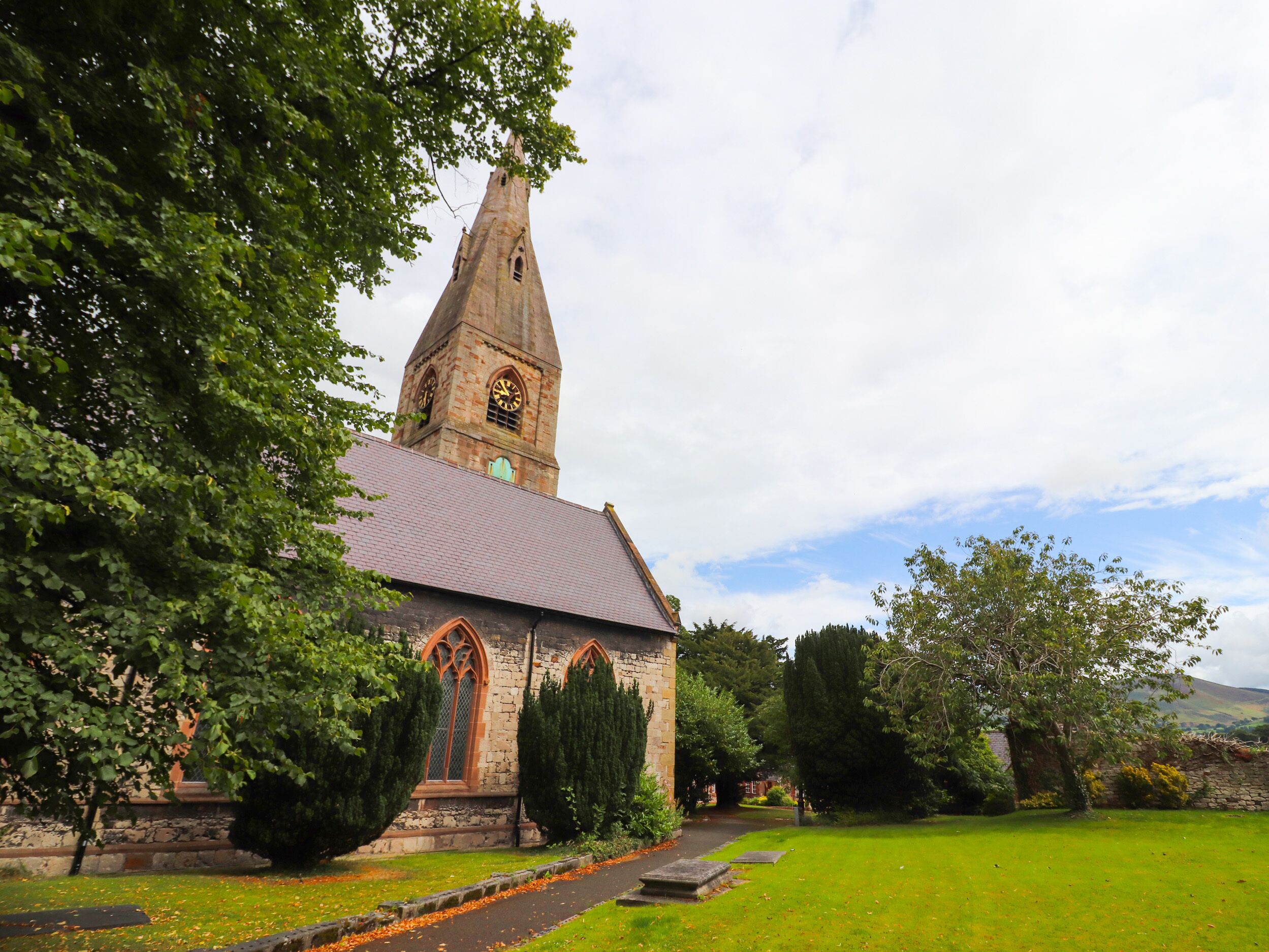 A church with a tall steeple, stone walls, and a pathway leading to the entrance.