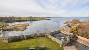 A riverside property with a grassy lawn, picnic tables, and a wooden fence. - Host & Stay | The Watchtower (Waren Mill)