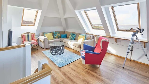 A loft-style room with a high ceiling, skylights, a sofa, armchairs, a coffee table, and a tripod. - Host & Stay | The Watchtower (Waren Mill)